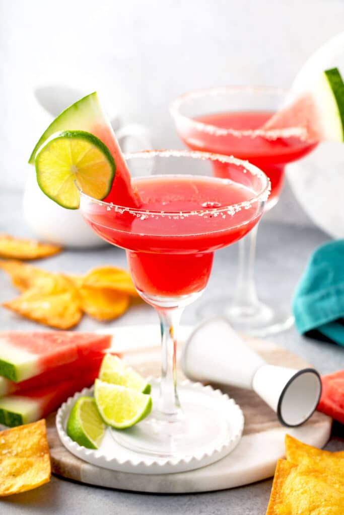 Two margarita glasses with salt on the rim filled with watermelon margarita and garnished with lime juice and fresh watermelon wedge