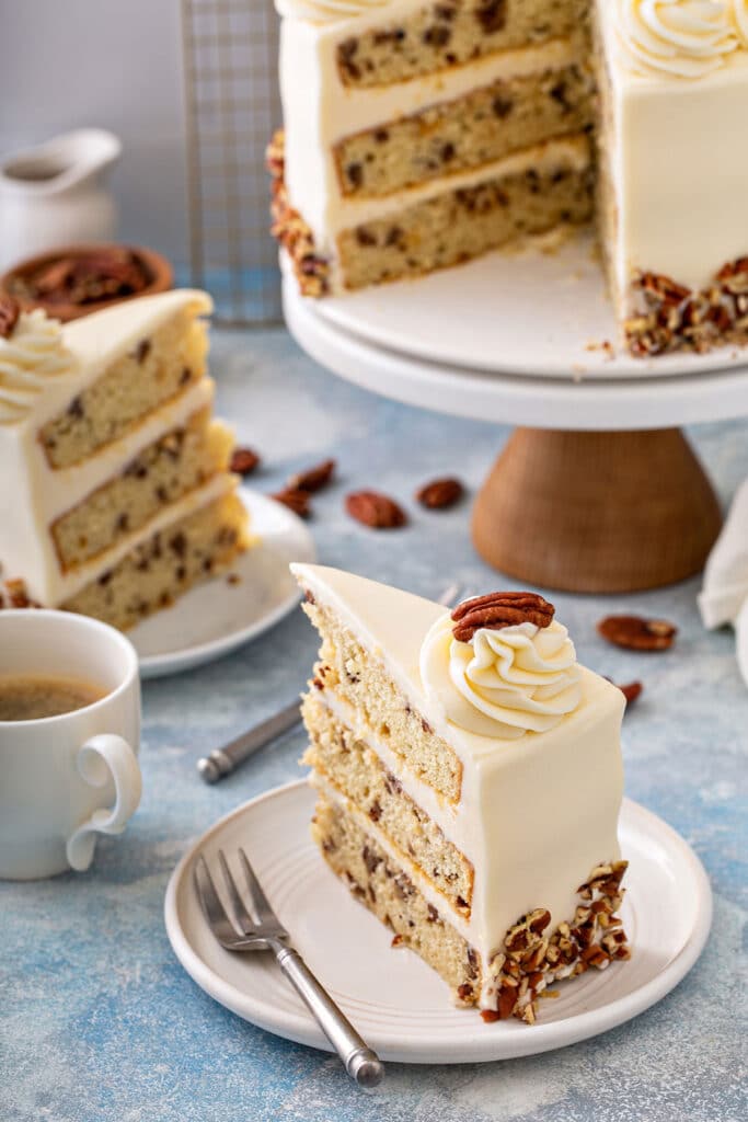 Slices of layered vanilla cake studded with buttered pecans frosted with cream cheese frosting on a white plate