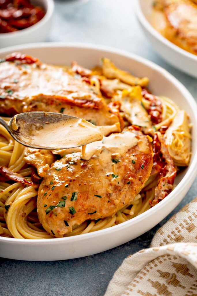 Creamy sun dried tomato sauce is poured over juicy golden brown chicken breast on a bed of pasta.
