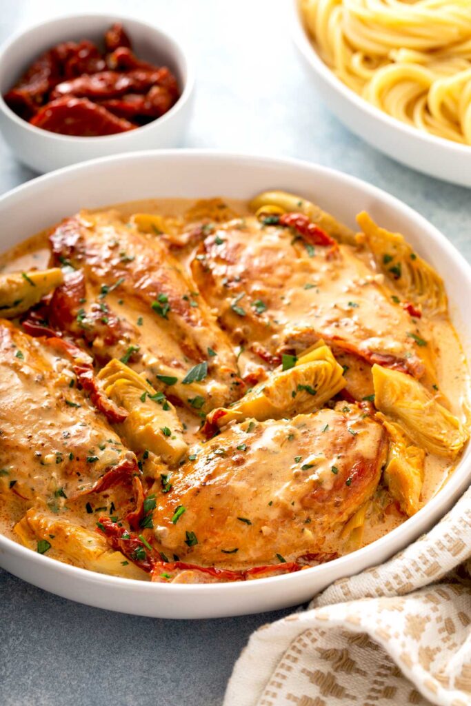 Chicken breast in a creamy sauce made with sun dried tomatoes and artichokes on a white bowl