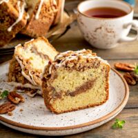 A slice of Sour Cream Coffee Cake loaded with a ribbon of cinnamon-sugar strudel running through the middle, pecans, cinnamon-sugar crumb topping and drizzled with maple glaze