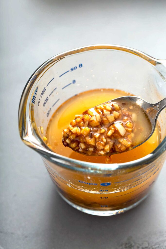 Showing minced ginger and garlic from the flavored Asian butter in a glass measuring cup.