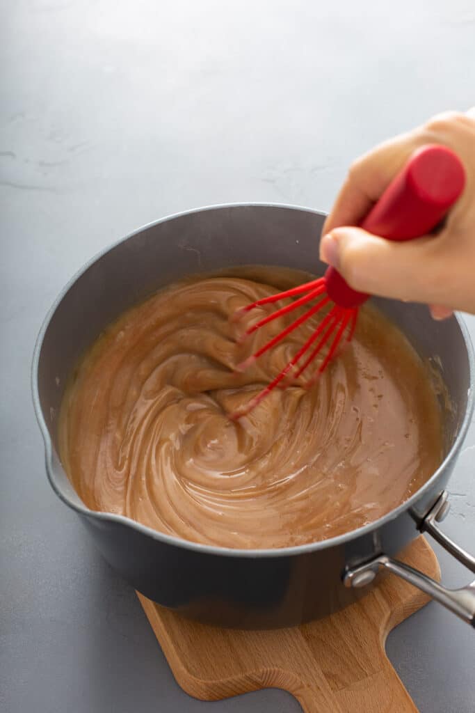 stiring caramel sauce with a red whisk
