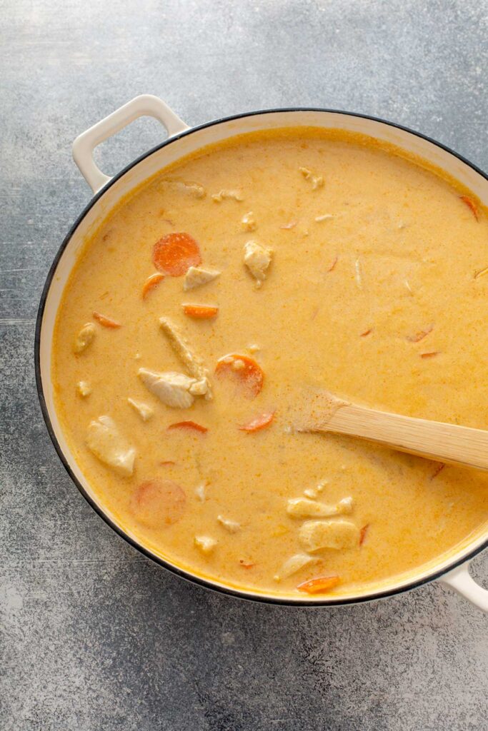 Chicken and carrots added into pot with thai curry sauce 