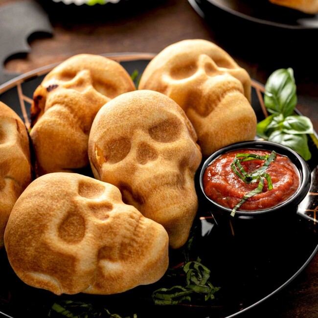 Golden brown baked pizza skulls serves on a black plate for Halloween