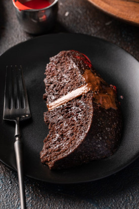 Slice of chocolate cake with chocolate buttercream on a black plate