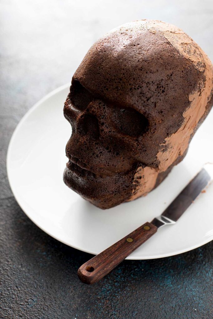Skull cake put together with a layer of chocolate buttercream on a white plate.