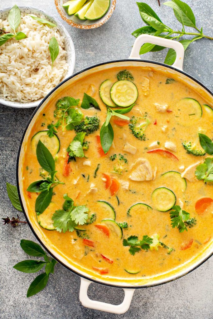 Coconut milk red curry with vegetables in a pot next to steamed rice