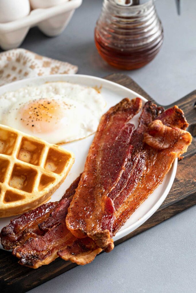 Crispy caramelized bacon in a white plate with sunny side fried egg and a waffle