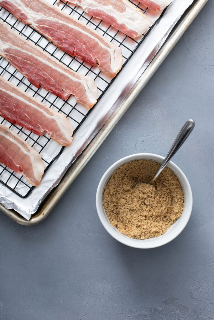 Bacon on a baking rack next to a bowl filled with brown sugar and pepper mixture.
