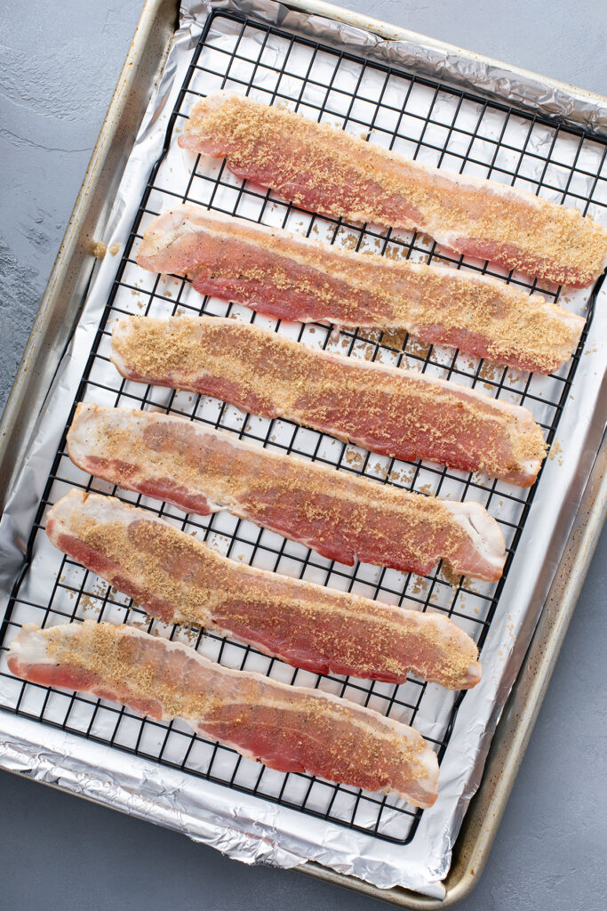 Bacon sprinkled with brown sugar and pepper on a baking rack.