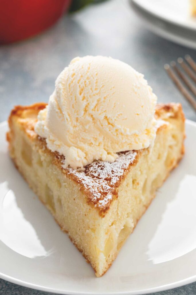 Slice of fresh apple cake served with ice cream on a white plate.