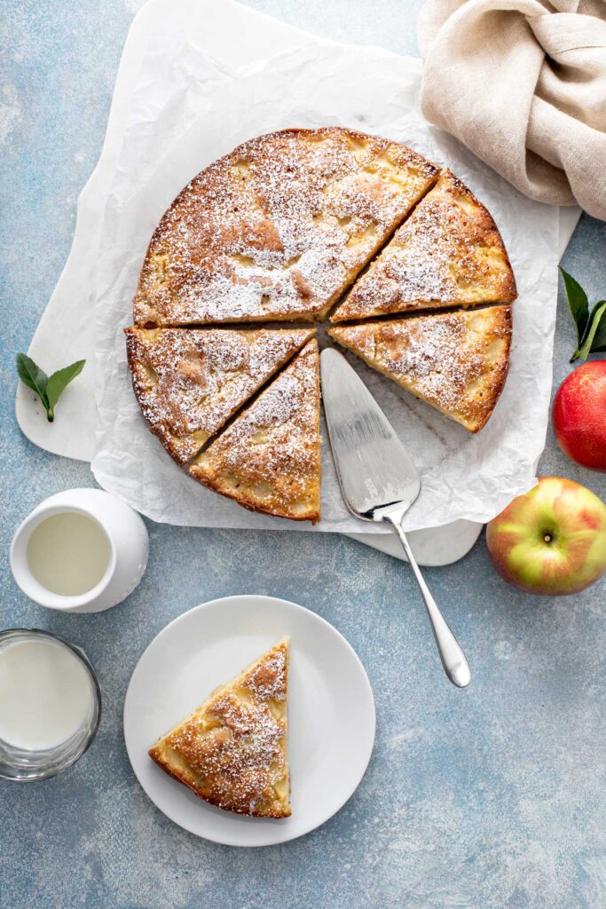 A whole fresh apple cake cut into big slices on a piece of parchment paper.