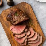 Sliced tenderloin of beef on a cutting board with a container of wine sauce next to it.