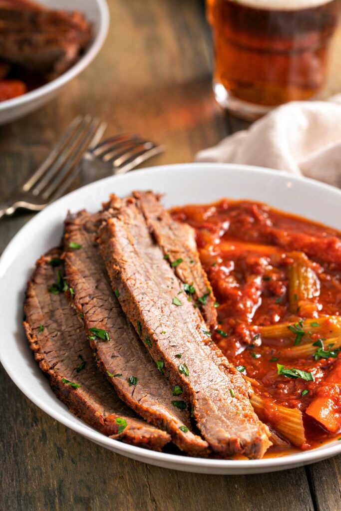 A plate with slices of brisket served with vegetables and sauce