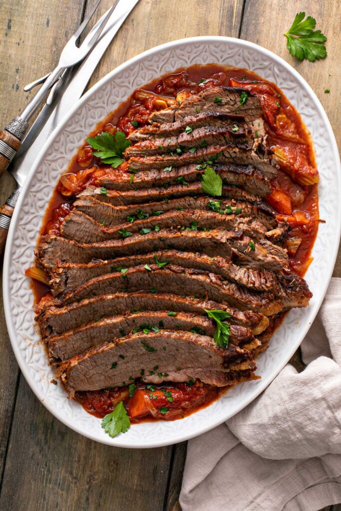 Top view of a platter filled with sliced brisket on top of carrots, onions and tomato based sauce