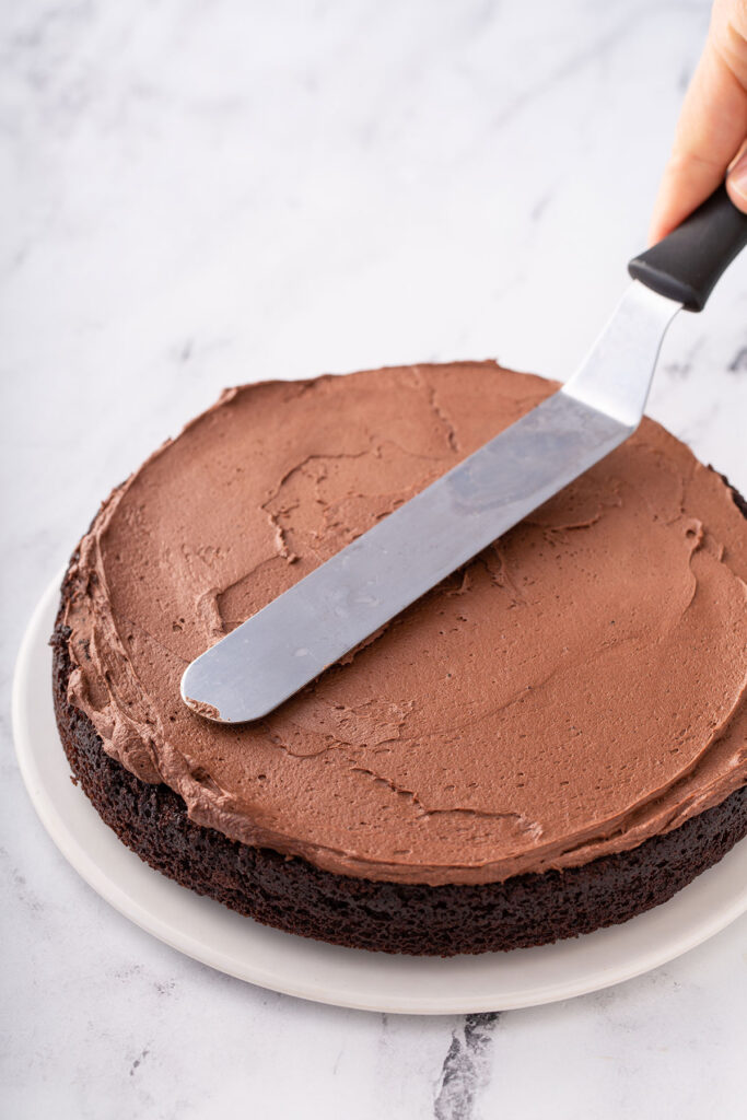 Chocolate buttercream icing mixed together and being smoothed onto chocolate cake. 