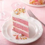 Slice of layered pink champagne cake with swiss meringue buttercream on a white plate