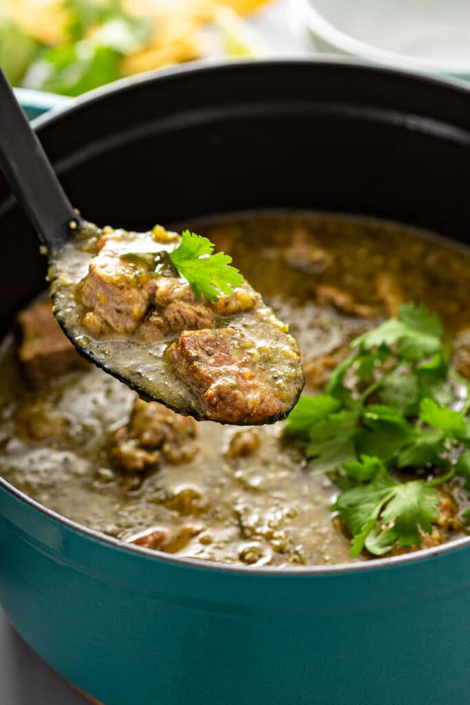 A big spoonful of pork in chile verde sauce lifted from a Dutch oven pot