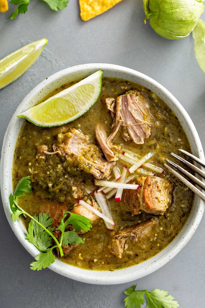 A bowl of pork chile verde stew with pieces of pork so tender that are getting shred by a fork 