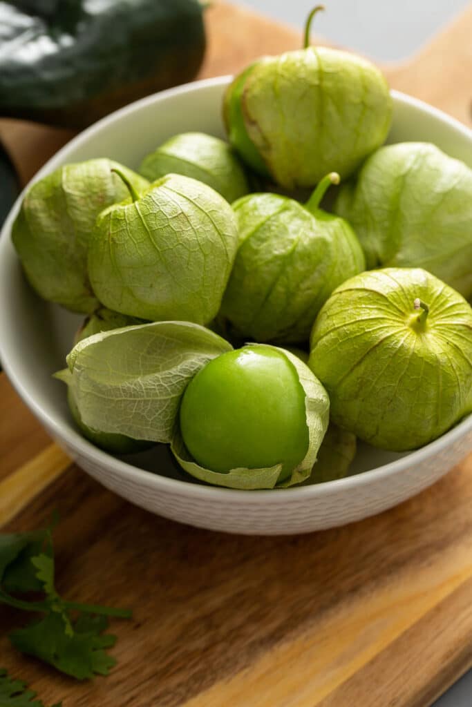 A white bowl filled with fresh tomatillos in their husk