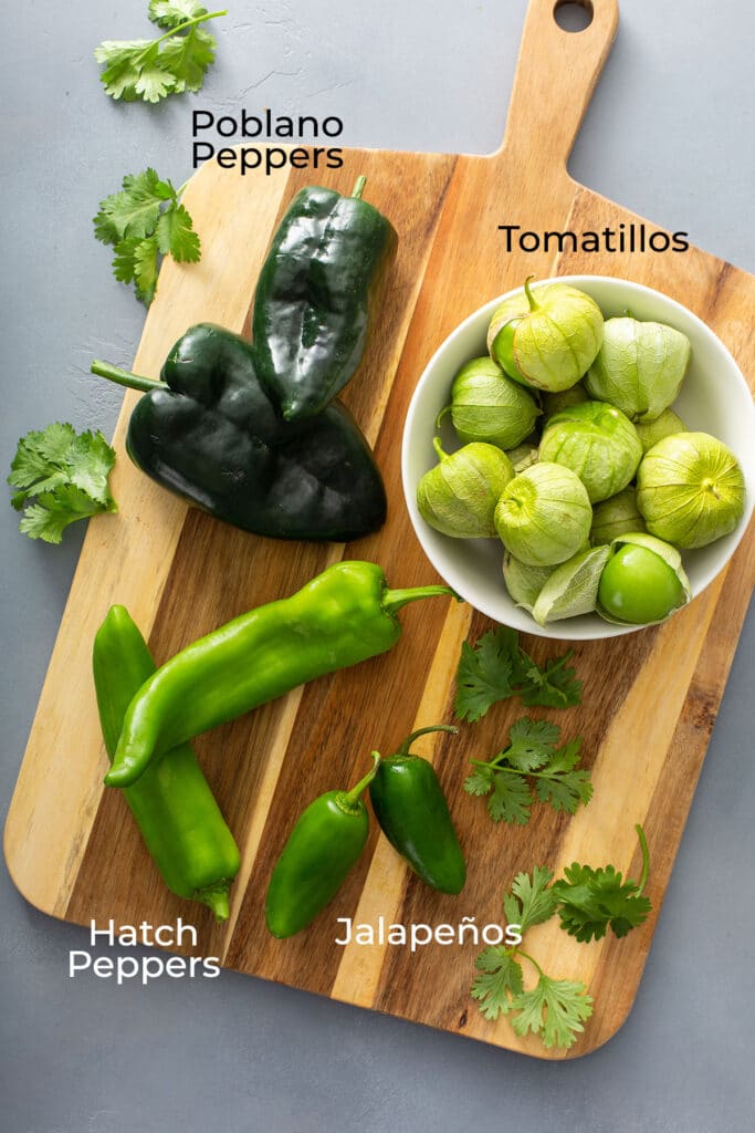 Fresh tomatillos, fresh poblano peppers, hatch peppers and jalapeños on a cutting board.