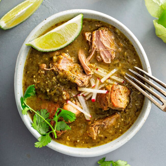 tender pieces of stewed pork in chile verde sauce getting shred with a fork