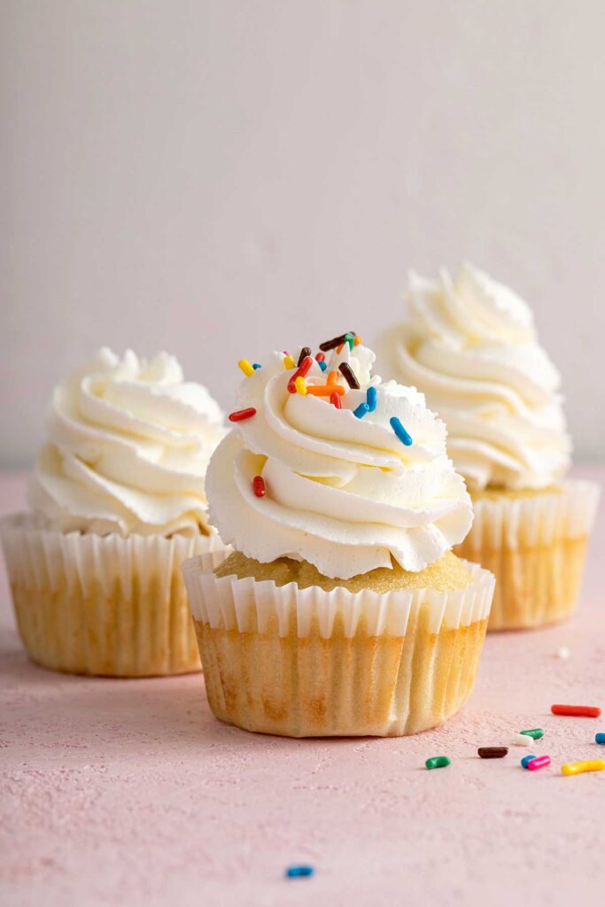 A vanilla cupcake frosted with silky and smooth Swiss meringue buttercream frosting and decorated with colorful sprinkles.