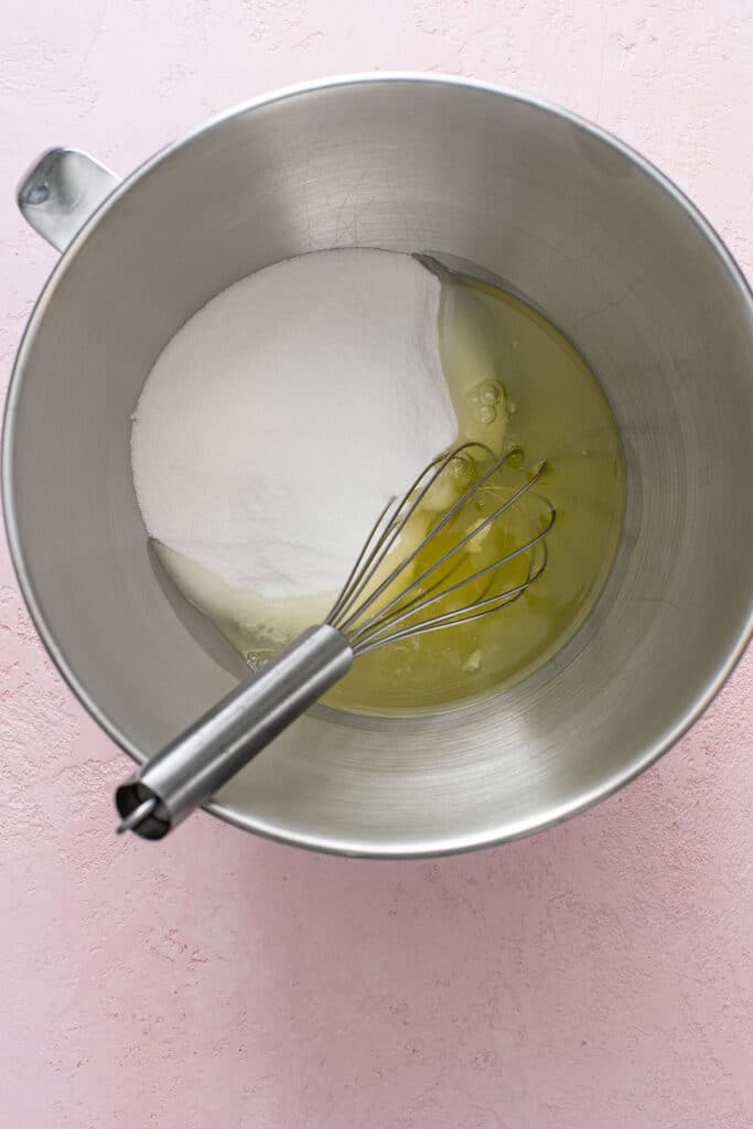 Step by step photos on how to make Swiss buttercream. A clean mixing bowl with egg whites and granulated sugar
