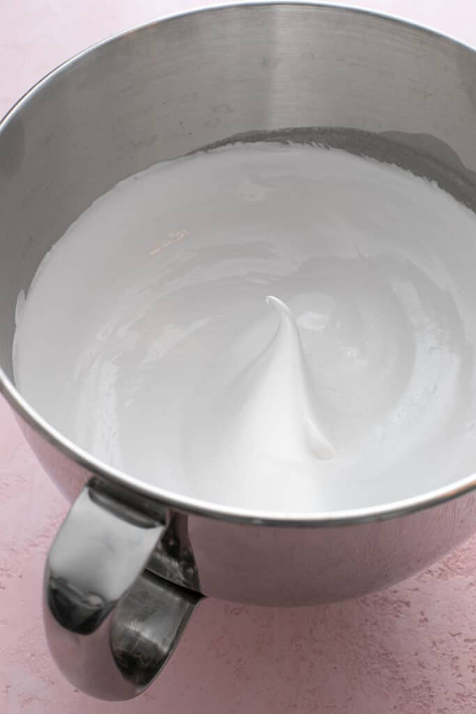 A metal mixing bowl with gg white meringue that has reached stiff peaks