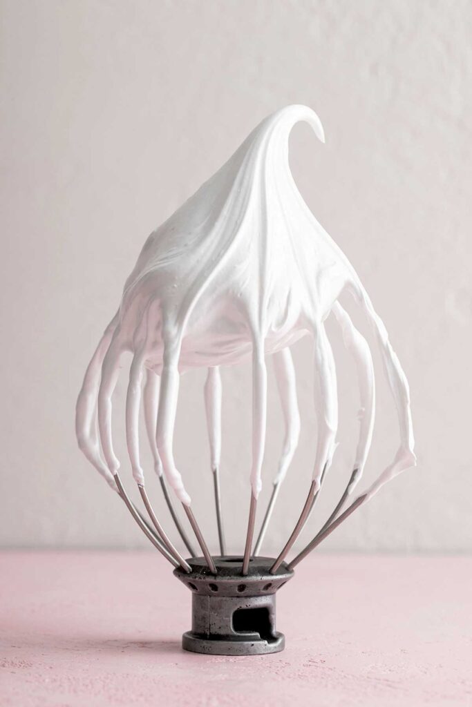 A whisk showing meringue that have reached stiff peaks