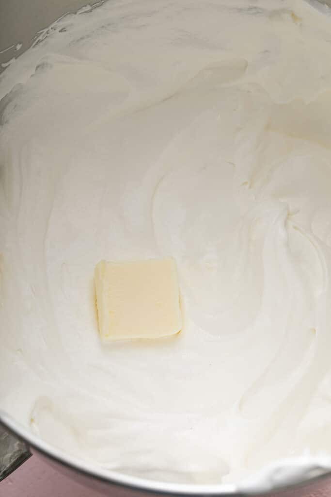 Step by step photos on how to make Swiss buttercream - meringue with a pad of butter in a mixing bowl