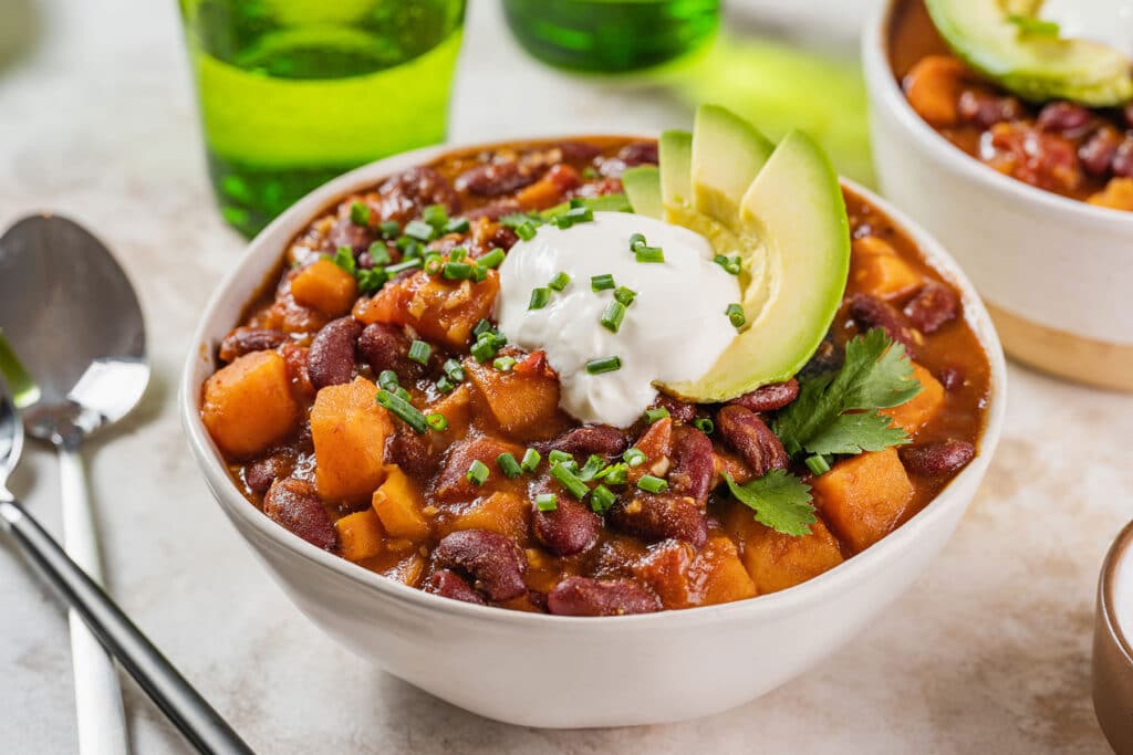 Vegetable chili topped with avocados and sour cream served in a white bowl.
