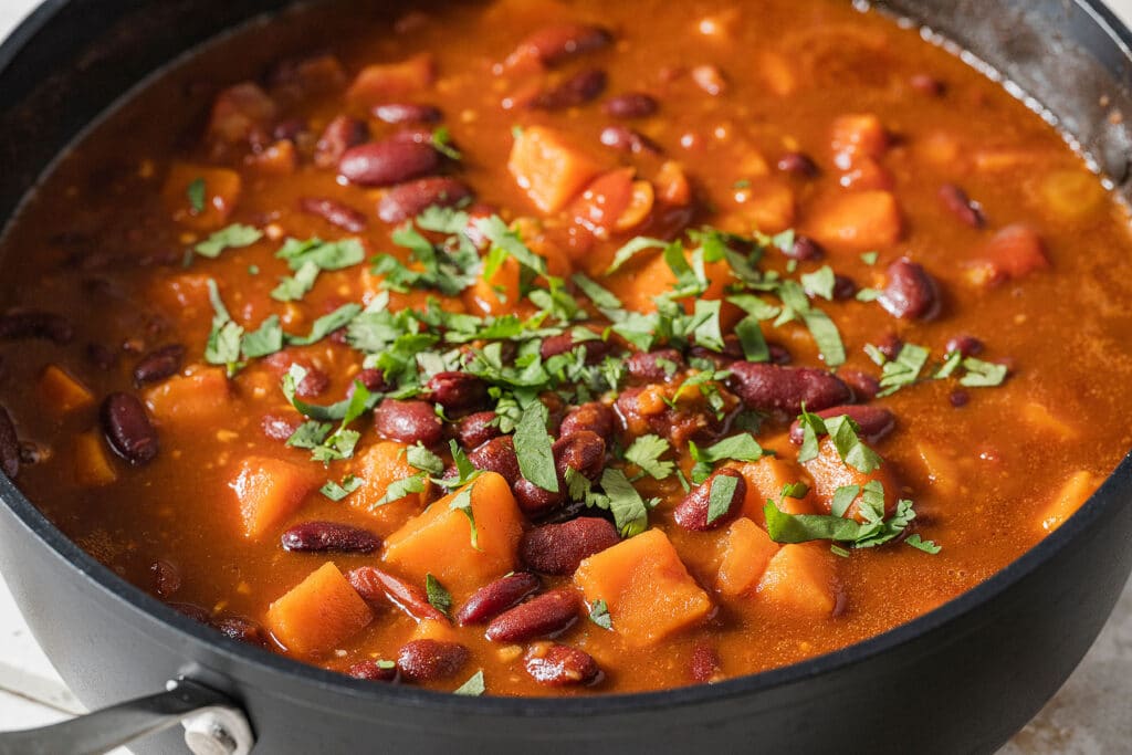 Chili with beans and sweet potatoes simmering in a pot and garnished with cilantro