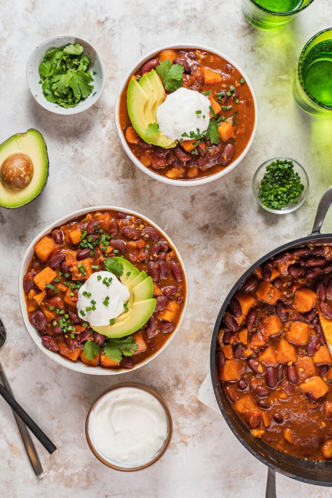 Bowls of vegetarian chili next to a pot of chili and toppings