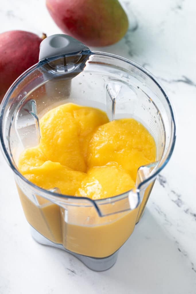 Thick and creamy mango smoothy in the glass of a blender.