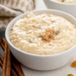 Creamy arroz con leche or Spanish rice pudding with golden raisins and sprinkled with ground cinnamon served in a dessert bowl.