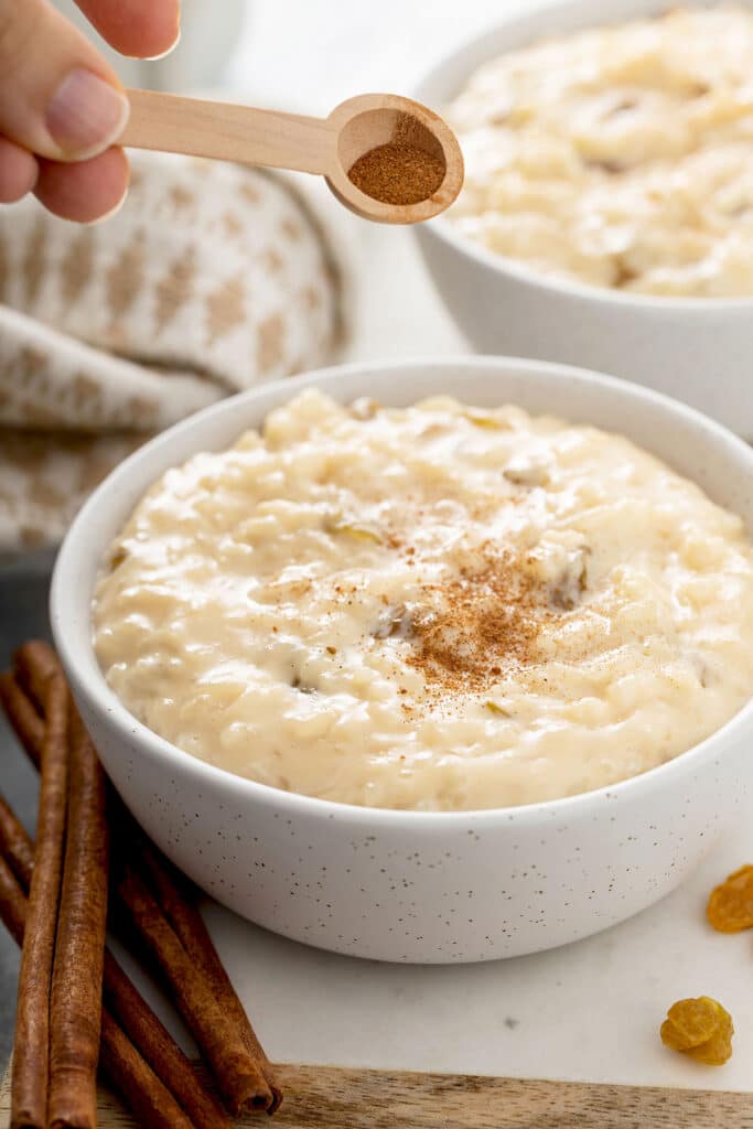 Ground cinnamon getting sprinkled on top of a bowl filled with creamy Spanish rice pudding aka arroz con leche.