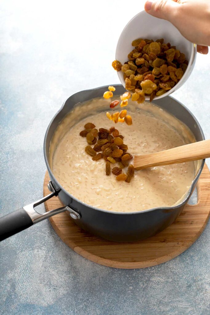 Golden raisins are being added to a pot of creamy arroz con leche (rice pudding)