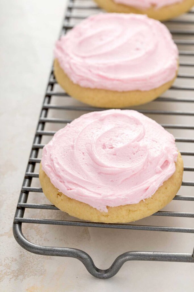 Close up of pink frosted sugar cookies on a cooling rack.