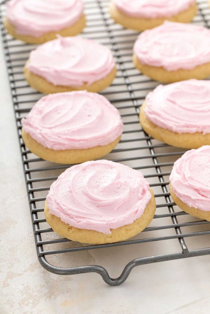 large sugar cookies with pink frosting on a cooling rack.