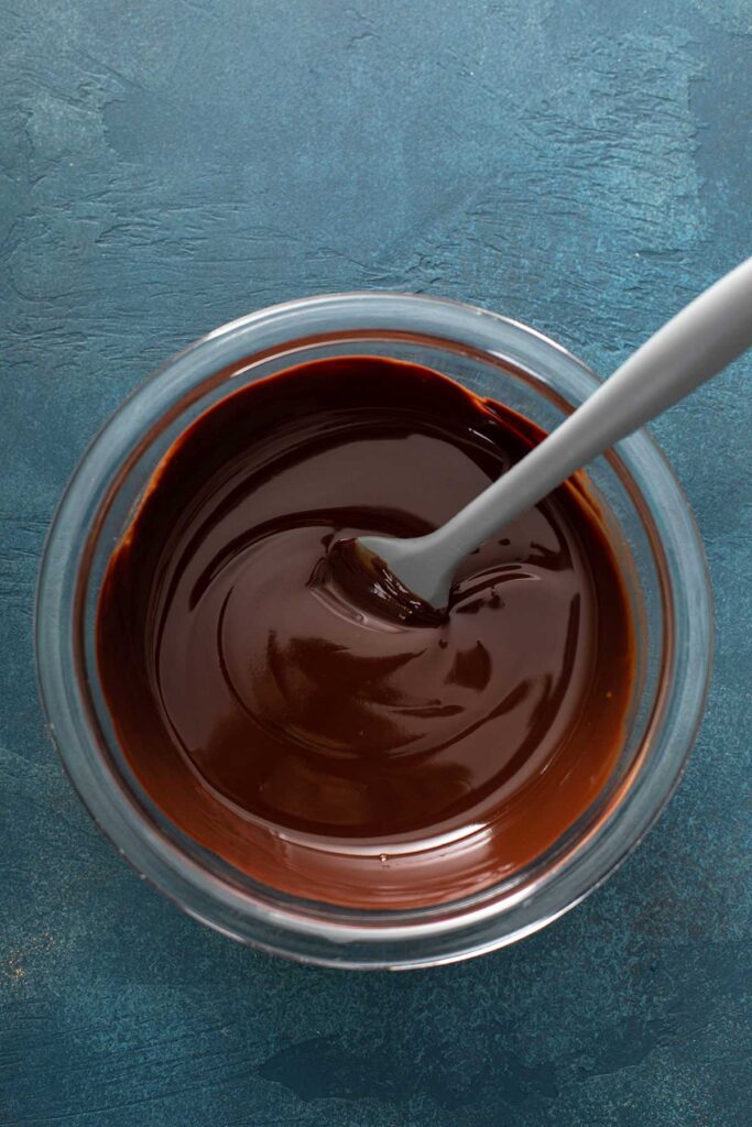 melted chocolate and butter in a clear mixing bowl with a gray spatula