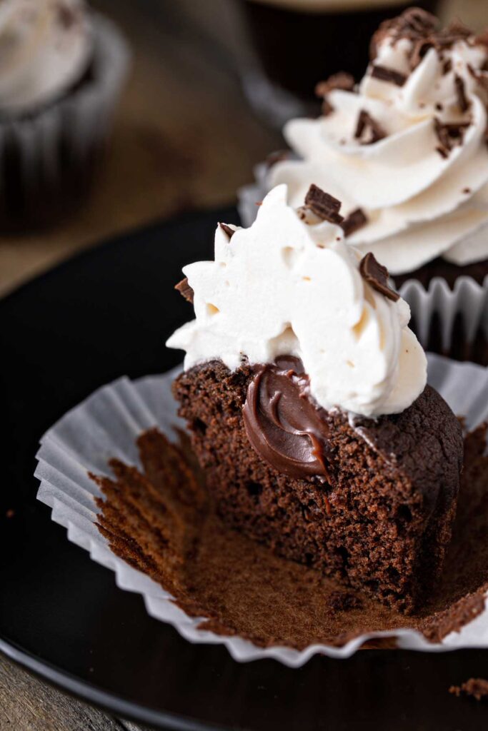 Moist Guinness chocolate cupcake with whipped frosting, cut in half showing it's ganache filling