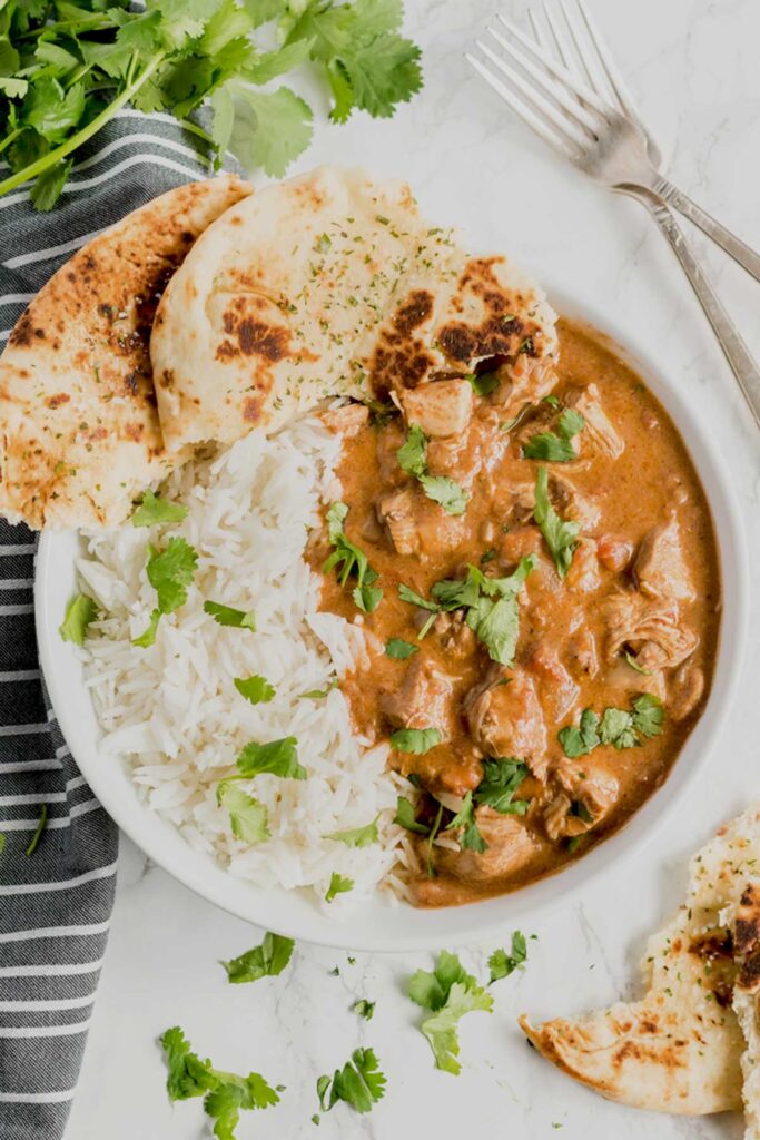 Indian butter chicken curry served with rice and naan bread on a white bowl.