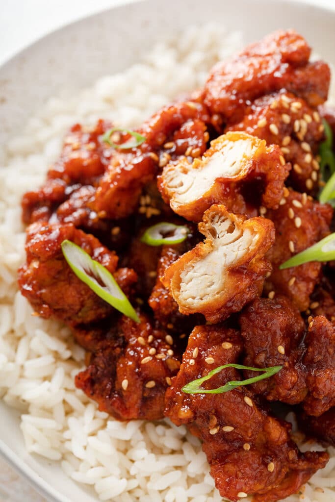 Korean fried chicken over rice and a small piece of chicken cut up to show its juicy interior and the crispy coating.