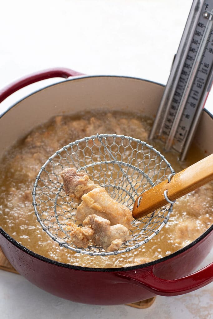 Lightly golden brown boneless chicken pieces getting lift from a pot of hot oil.