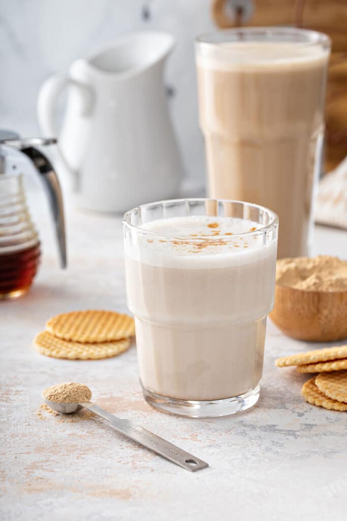 In this image, a glass with maca latte and a larger glass filled with maca latte made with cacao and turmeric