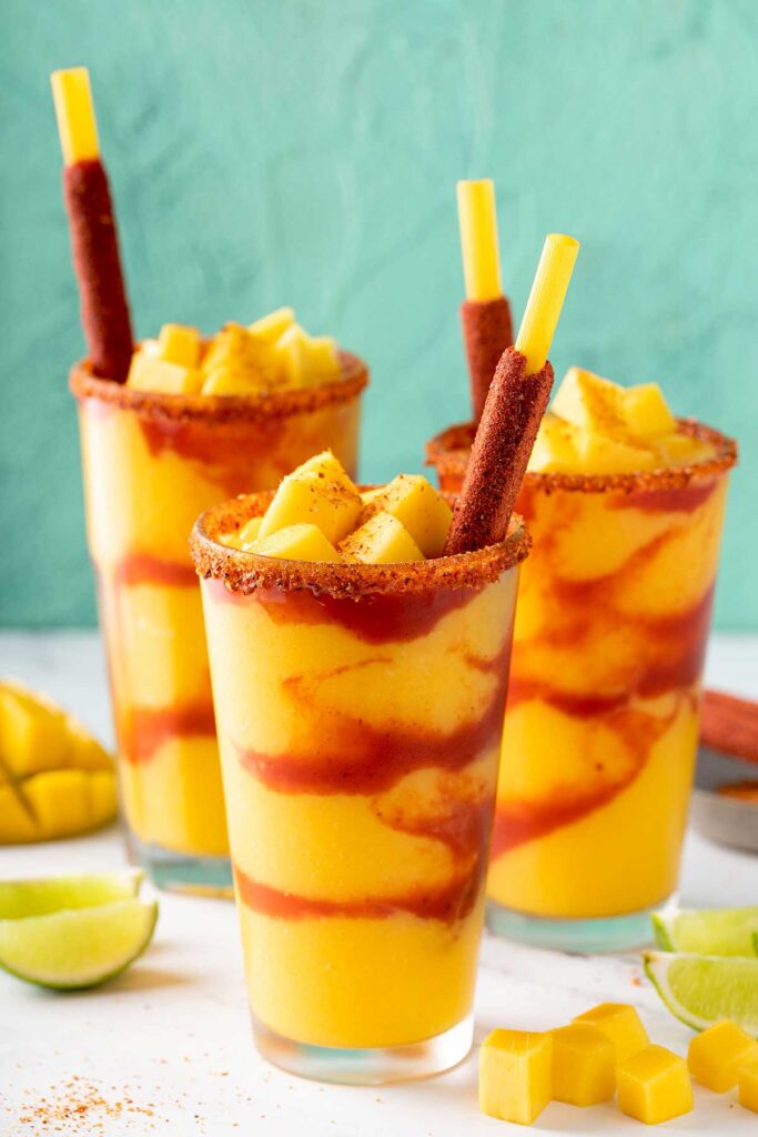 Glasses filled with mango smoothie layered with spicy sauce and topped with mango chunks and Tajin. Served with a tamarind candy straw.