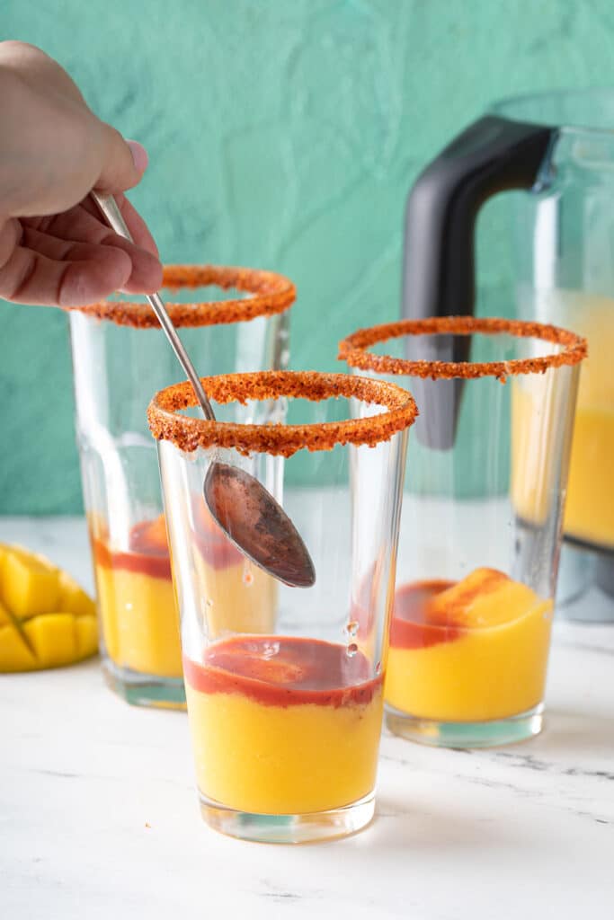 adding chamoy sauce over the mango smoothie with a spoon