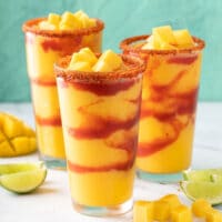Three glasses filled with frozen mocktail made from mango and layered with spicy Mexican sauce.
